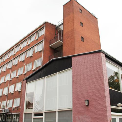 Groot, rood bakstenen kantoorgebouw met meerdere verdiepingen en een ingekrompde, moderne ingang.