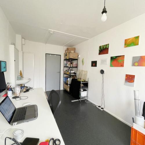 Moderne werkstudio met een lang wit bureau, elektronica, en een wand vol kleurrijke abstracte schilderijen.