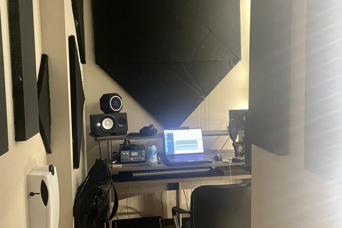 Een moderne presentatiehoek met een tafel, monitor, audioapparatuur en een groot zwart projectie- of muurpaneel.