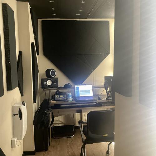 Een moderne presentatiehoek met een tafel, monitor, audioapparatuur en een groot zwart projectie- of muurpaneel.