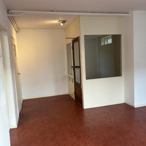 Interieur van een kale kamer met rode vloer, witte muren en een grote spiegel op de muur.