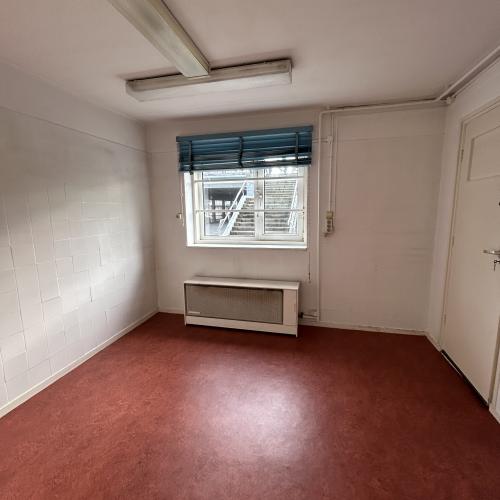 Leeg woonkamerinterieur met roodbruine vloer, witte muren en een raam met rolgorden.