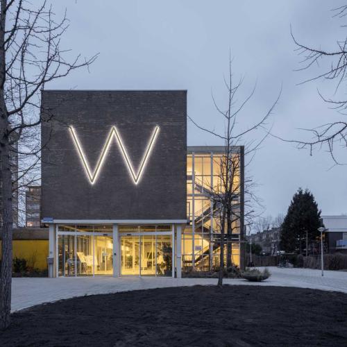 Modern gebouw met een grote, verlichte 'W'-initial in de gevel, gezien bij schemering.