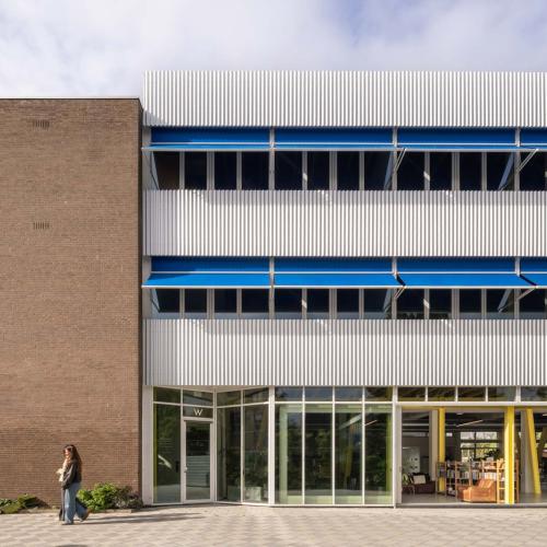 Modern kantoorgebouw met beige en wit gevelmateriaal, blauwe raamomlijstingen en een glazen etalage op de begane grond.