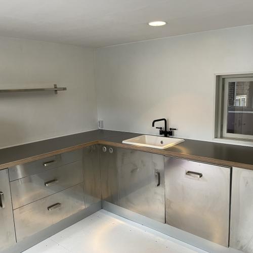 Modern, minimalistische keuken met roestvrijstalen kasten en aanrechtblad, en een kleine gootsteen.