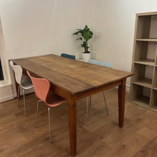Houten eettafel met vier stoelen: twee witte en twee oranjerode stoelen staan eromheen.
