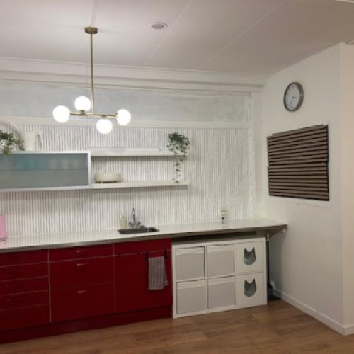 Moderne keuken: rood onderkast, witte metro-tegels en zwevende planken. De ruimte wordt verlicht door een kroonluchter.