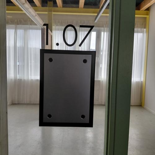 De ingang van een ruimte, voorzien van een groot zwart bord en de nummers 1.07 erboven, in een modern interieur.