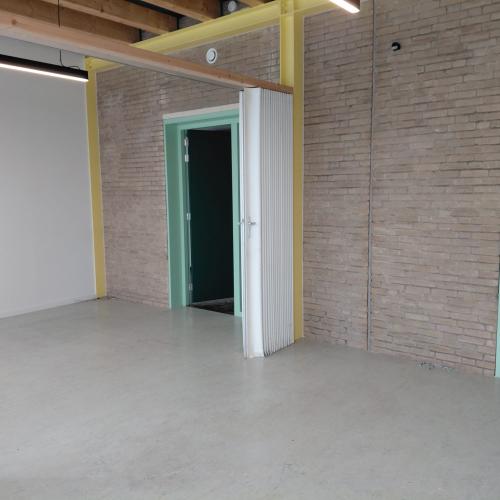 Interieur van een lege, moderne ruimte met grijze vloer, contrasterende muren en meerdere deuren in verschillende kleuren.