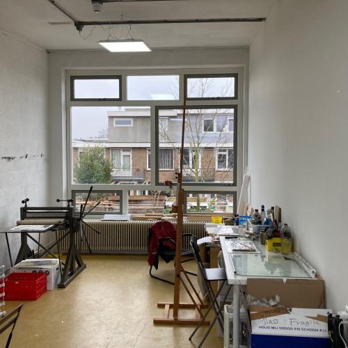 Interieur van een stoffige werkruimte met grote ramen en diverse spullen op de vloer.