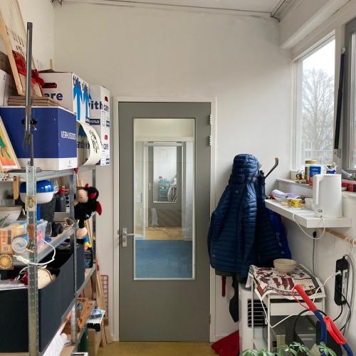 Overzicht van een winkel met planken, een deur en een raam, vol met producten.