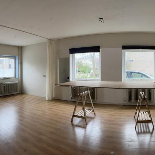 Luxe, lege woonruimte met licht parket, grote ramen en minimalistische inbouwmeubels. Twee houten decorstukken staan centraal.
