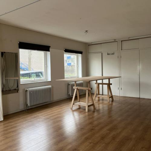 Lege vergaderruimte met een lange tafel en stoelen in het midden. Links ramen en rechts een reeks witte deuren.