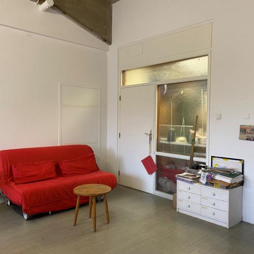 Moderne, lichte woonkamer met een rode bank, een klein bijzettafeltje, en een witte ladekast naast een glazen kast.