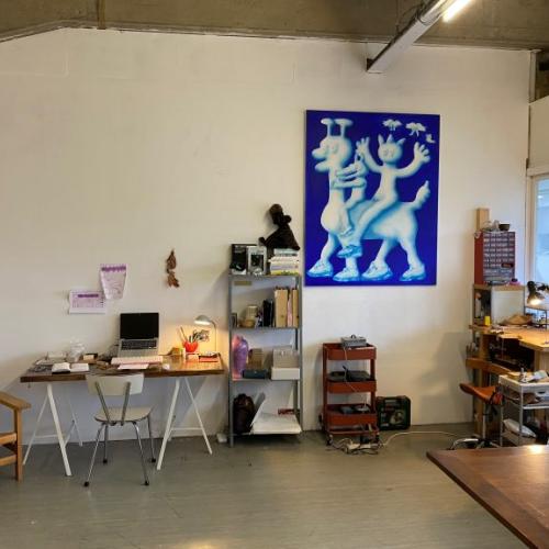 Grote, lege, kunstgalerie met wit plafond, diverse kunstwerken en een werktafel.