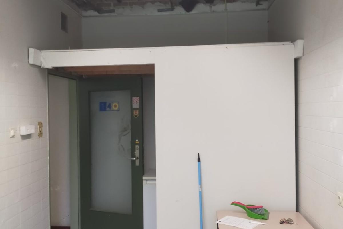 Interieurfoto van een lege, kale kamer met een ingedeelde doorgang en een tijdelijke werktafel.