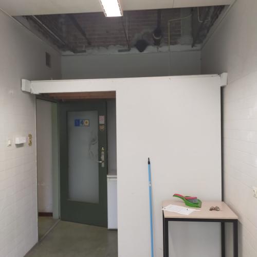 Interieurfoto van een lege, kale kamer met een ingedeelde doorgang en een tijdelijke werktafel.