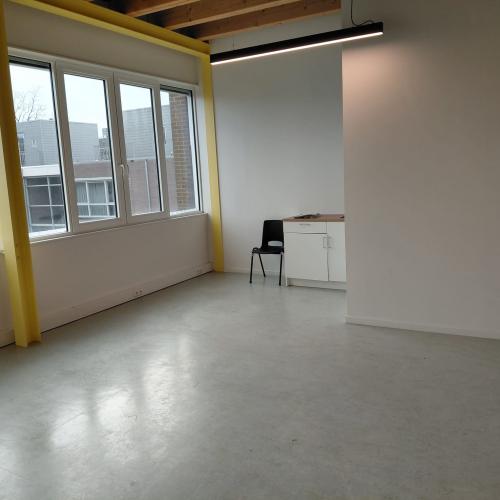 Modern, licht ingericht interieur met grote ramen, een minimalistische muur en een klein kastje.