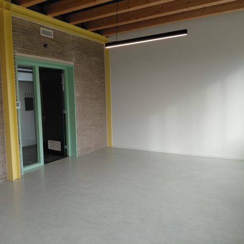 Groot, leeg en modern binnenruimte met lichte vloer, bakstenen muur en een glazen deur.