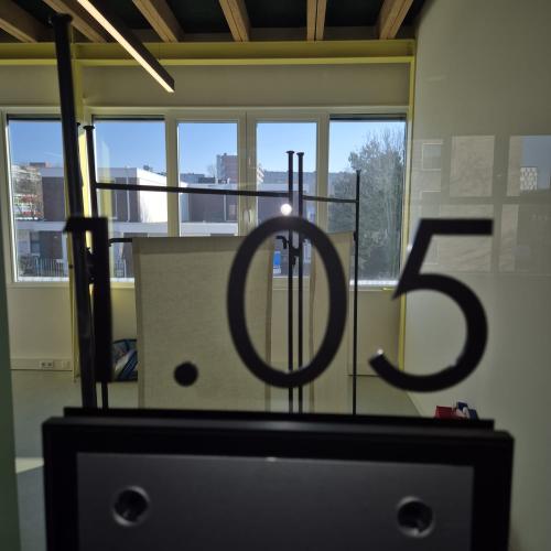 Een decoratief hangend nummer '05' op een donker meubelstuk bij een raam.