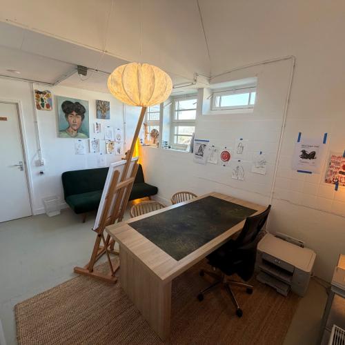 Interieur van een lichte, minimalistische ruimte met een bureau, een klok in een globe-vormige kap en diverse kunstwerken.