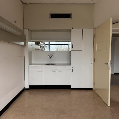 Moderne badkamer met witte wastafel, ingebouwde kastenwand en een openstaande witte deur.
