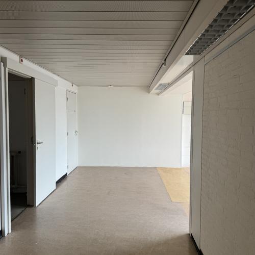 Lege, moderne kamer met witte muren, een lichte vloer en een zichtbaar plafond met ventilatie en rijen deuren.