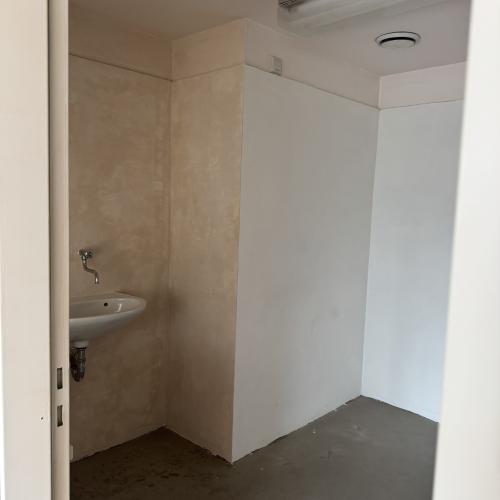 Een kleine, moderne badkamer met een wit wastafel en kraan, en een lege, witte hoek.