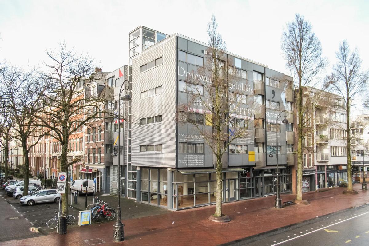 Moderne kantoorgevels naast oude gebouwen, met voor een breed trottoir en parkeerplaats.