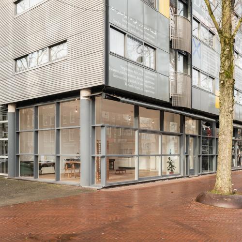 Moderne architectuur met een ingeklemd glazen winkelgebied op een roodbruine stoep, naast een kale boom.