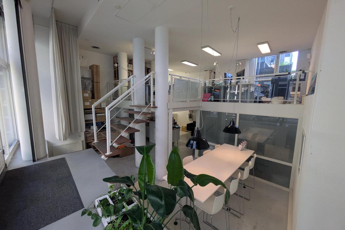 Modern kantoorinterieur met een balie, trap, grote ramen en plantdecoratie.