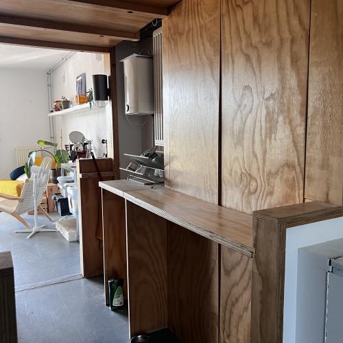 Houten kastenwand en bar die openstaan naar een lichte, moderne keuken met witte kasten en apparatuur.