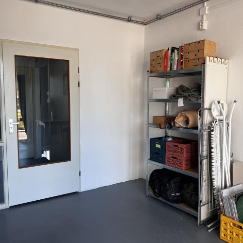 Binnen shot van lege ruimte met witte muren, glazen deur en een hoge, open plank met diverse objecten.
