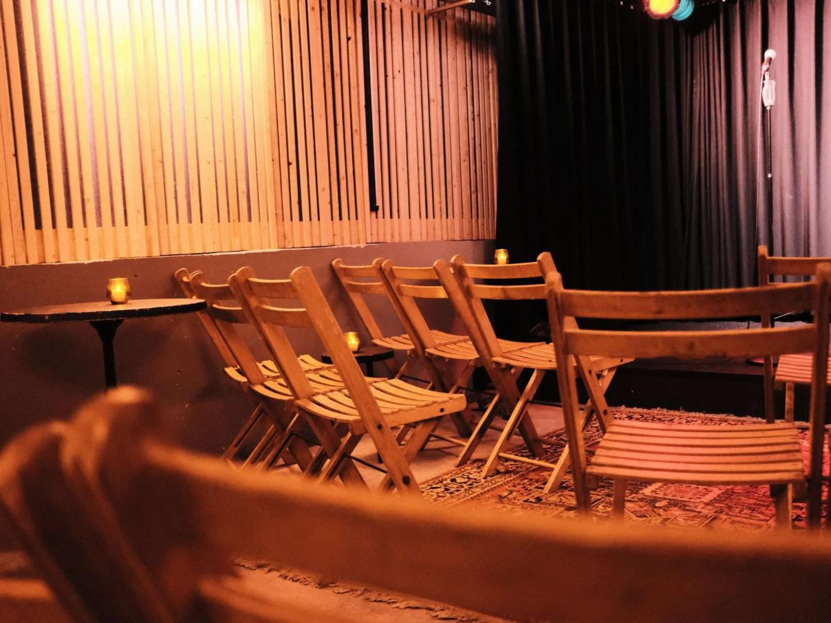 Een auditorium met rijen houten stoelen, geflankeerd door lichte en donkere gordijnen.