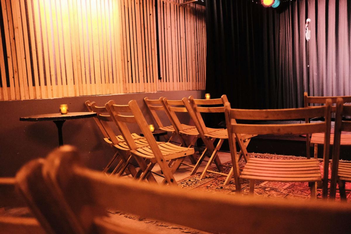 Een auditorium met rijen houten stoelen, geflankeerd door lichte en donkere gordijnen.