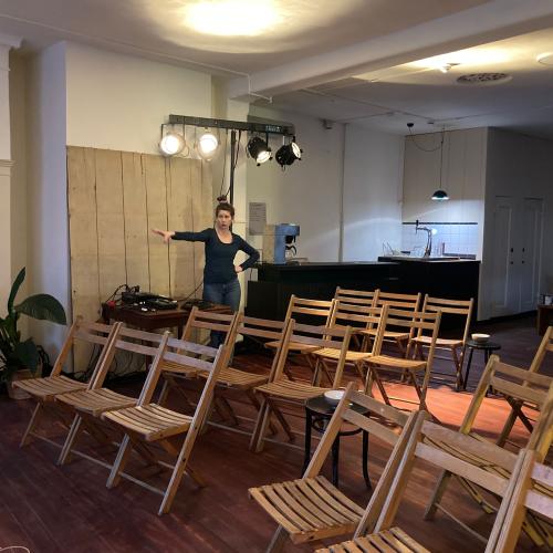Binnenruimte met opgestelde stoelen en een vrouw die een presentatie geeft bij een podium.