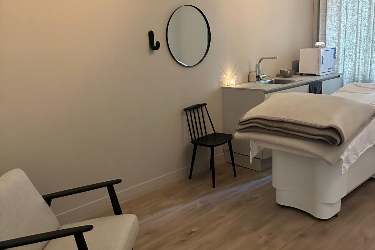 Interieurfoto van een spa-kamer met een behandeltafel, twee fauteuils en een rond spiegel aan de muur.