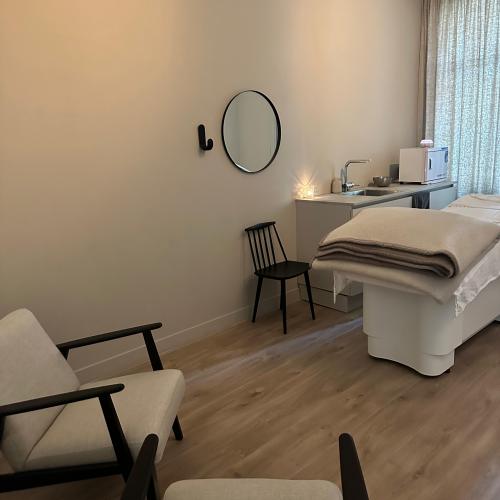 Interieurfoto van een spa-kamer met een behandeltafel, twee fauteuils en een rond spiegel aan de muur.