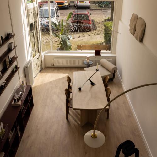 Lichte woonkamer met grote raampartij die uitkijkt op een historische straat. In de ruimte staat een eettafel.