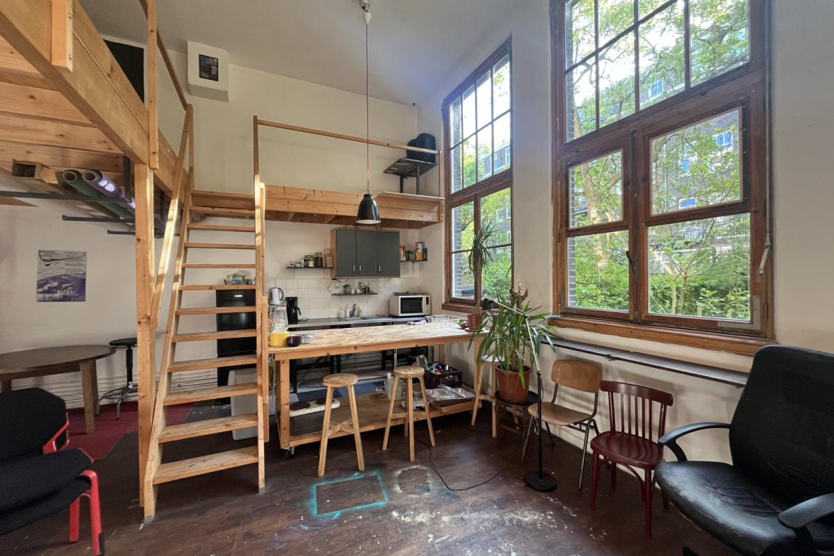 Licht interieur met een houten trap, een keukenopstelling en grote ramen. De ruimte straalt een rustieke, open sfeer uit.