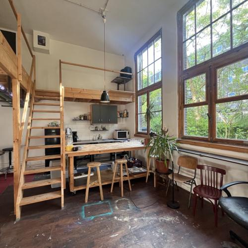 Licht interieur met een houten trap, een keukenopstelling en grote ramen. De ruimte straalt een rustieke, open sfeer uit.