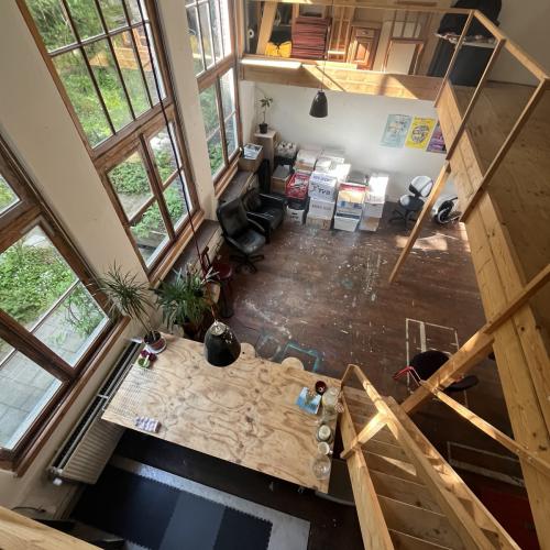 Uitzicht vanaf de trap naar een grote, lichte woonkamer met raampartijen en een lichte keukenaanrecht.