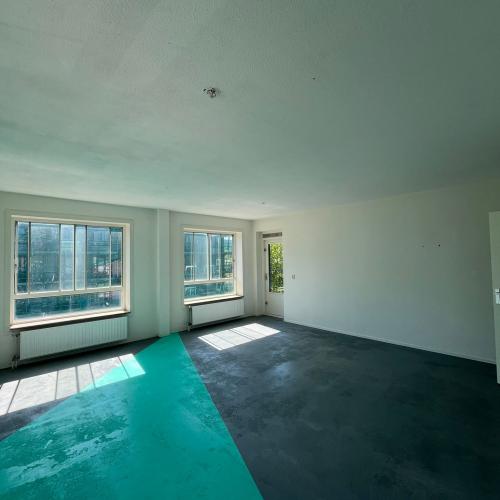 Modern interieur: een helder turquoise zwembad dat grenst aan een donkergekleurde, minimalistische kamer met ramen en veel natuurlijk licht.