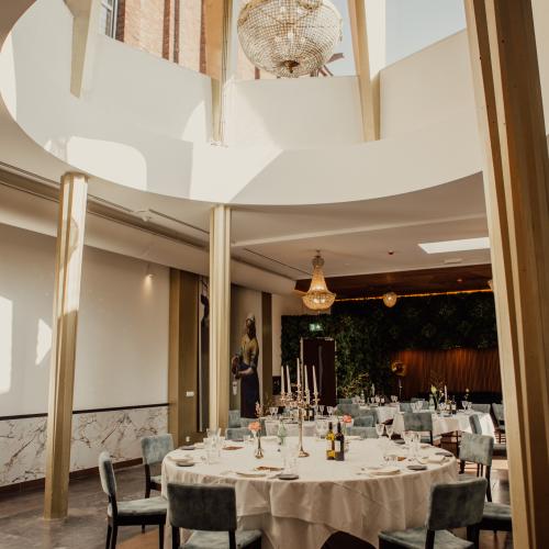 Interieurfoto van een luxe restaurant met een grote ronde architectonische opening, gedekte tafels en kristallen kroonluchter.