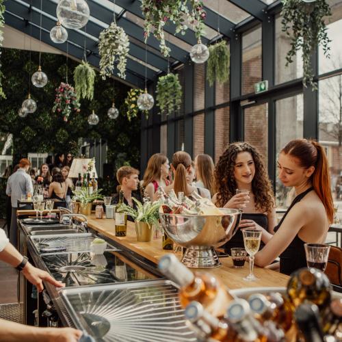 Een lichte winkel met hangplanten. Vrouwen bladeren door decoratieve waren achter een lange houten toonbank.