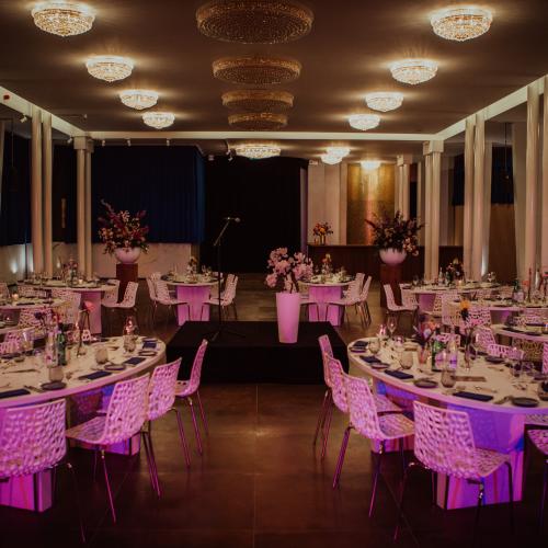 Grote, gedekte zaal met rechthoekige tafels en huurstoelen, klaar voor een evenement.