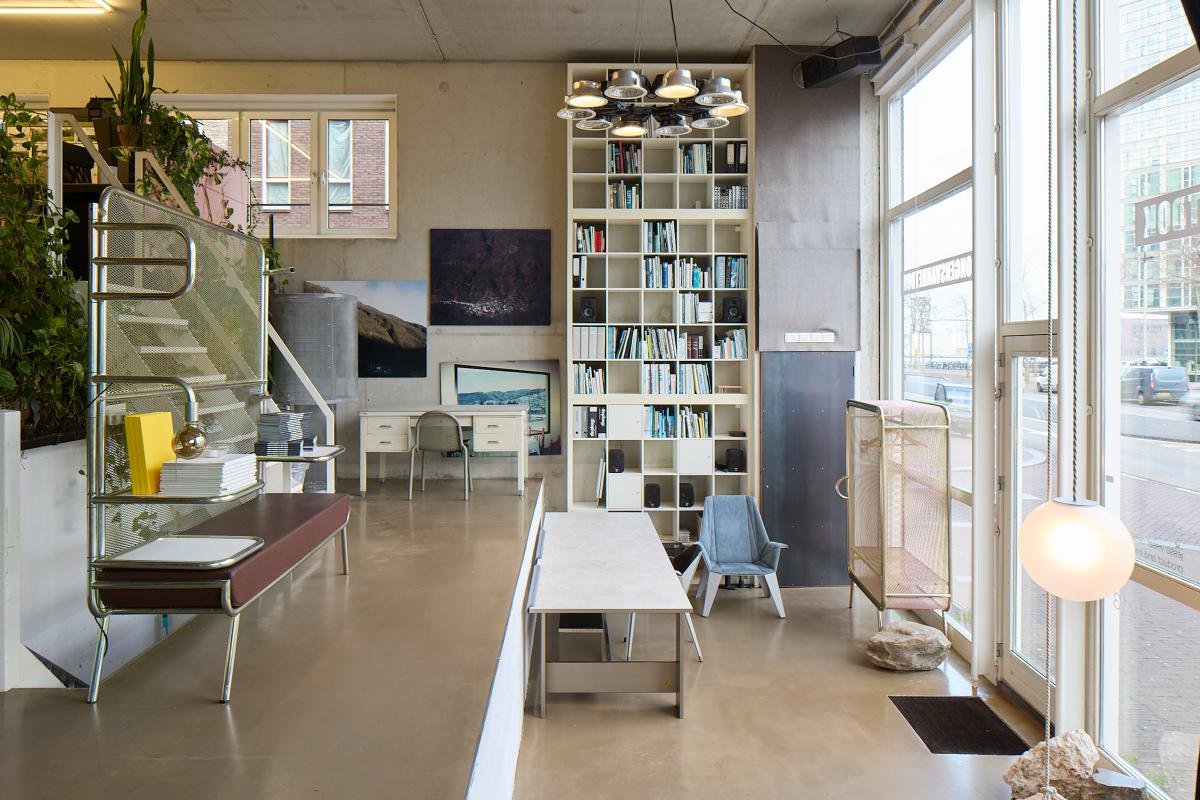 Interieurfoto van een moderne, zonnige ruimte met een boekenkast, trap en lange tafel.