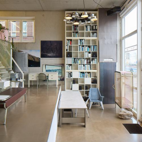 Interieurfoto van een moderne, zonnige ruimte met een boekenkast, trap en lange tafel.
