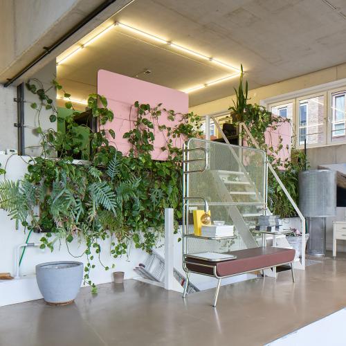 Moderne, lichte ontvangstruimte met veel groen, zachte roze accenten en een glazen balustrade.