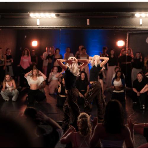 Een energieke menigte mensen danst en viert op een donkere, verlichte dansvloer tijdens een feest.